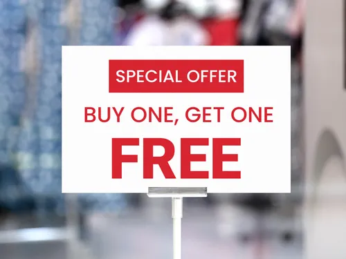 Bold foam board sign with a red and white design, featuring a "Buy One, Get One Free" special offer, displayed on a stand in a retail setting