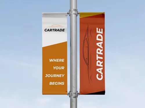 ​A single vertical pole banner with an orange design promoting a car trade event, mounted on a street pole in an urban environment
