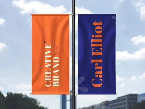 ​A single vertical pole banner featuring an orange and purple design with creative branding elements, mounted on a street pole in an urban environment