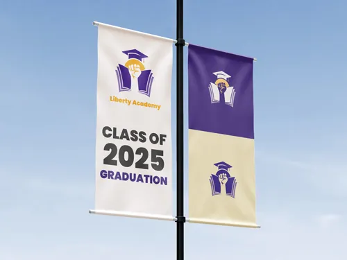 A vertical pole banner in purple and yellow colors with graduation-themed graphics, displayed on a street pole in an outdoor setting
