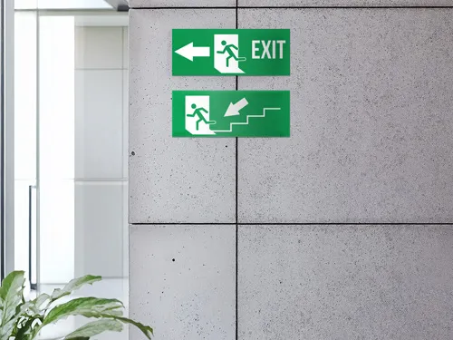 Durable styrene signs with green backgrounds and white emergency exit graphics, clearly indicating stair access and exit direction in a modern indoor setting