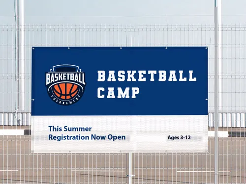 Basketball camp mesh banner on fence with registration open for ages 3-12 this summer.
