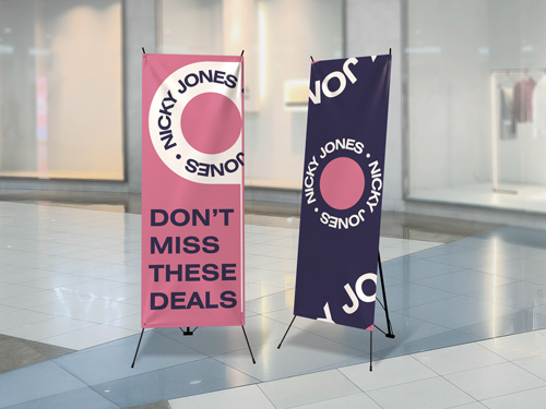 Two colorful Nicky Jones X-stand banners promoting deals in a modern indoor setting.